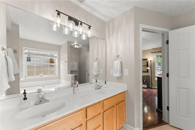 bathroom featuring a textured ceiling, a garden tub, double vanity, and a sink