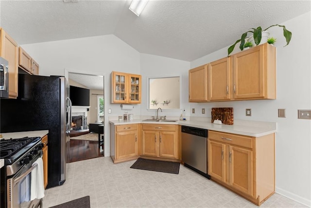 kitchen with a sink, a lit fireplace, appliances with stainless steel finishes, light countertops, and vaulted ceiling