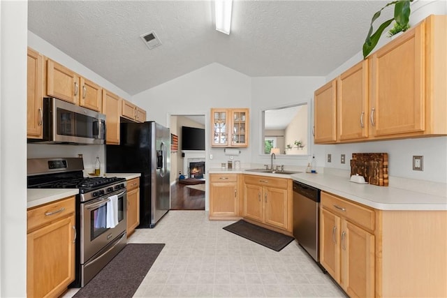 kitchen with light brown cabinetry, light countertops, lofted ceiling, appliances with stainless steel finishes, and a sink