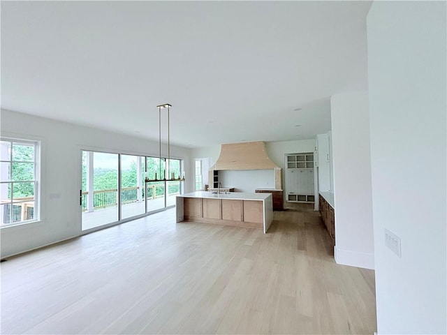 kitchen with open floor plan, light wood-style floors, a center island with sink, and wall chimney exhaust hood