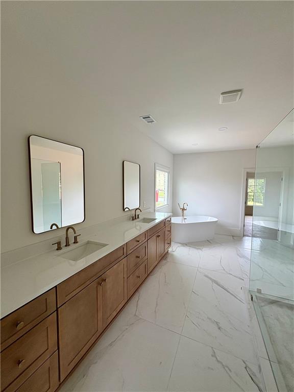 full bath with plenty of natural light, a freestanding bath, double vanity, and marble finish flooring