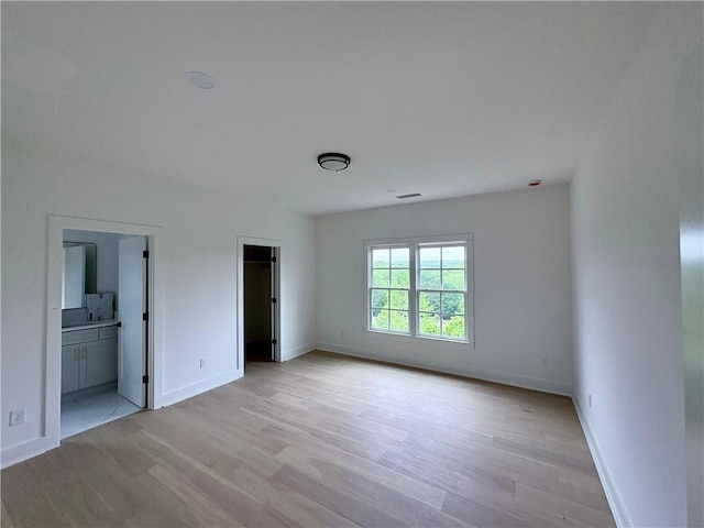 unfurnished bedroom with light wood finished floors, baseboards, and a walk in closet
