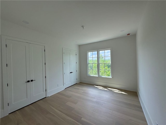 unfurnished bedroom featuring multiple closets, wood finished floors, and baseboards