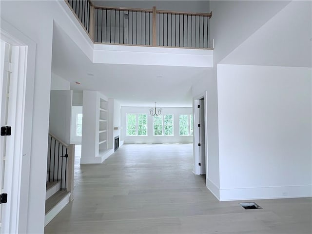 hall featuring a chandelier, a high ceiling, wood finished floors, baseboards, and built in features