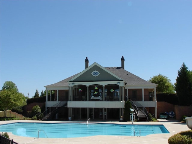 community pool with stairs, a sunroom, and fence