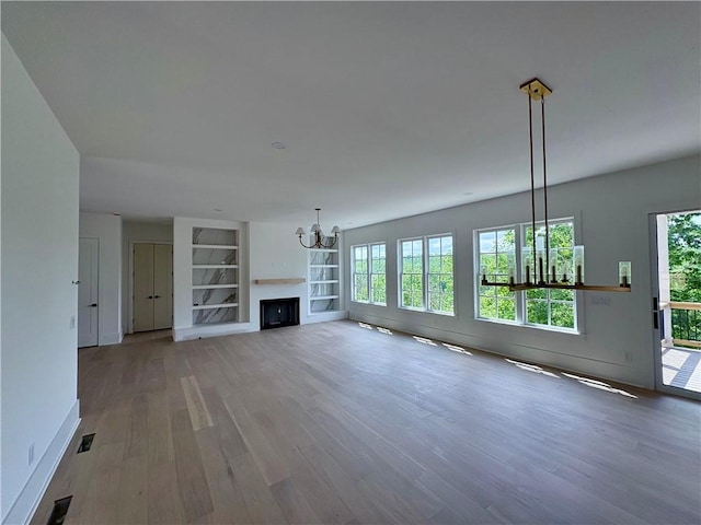 unfurnished living room featuring a chandelier, wood finished floors, built in shelves, and baseboards