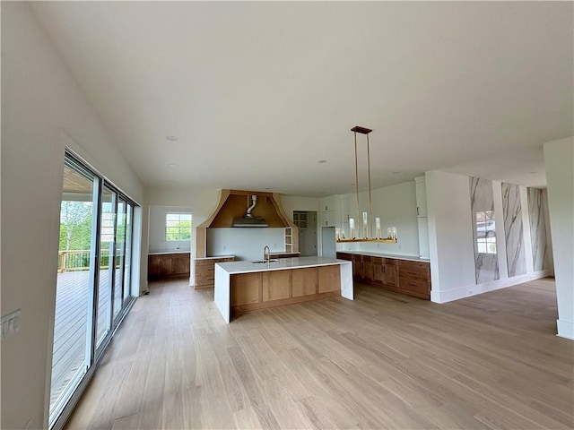 kitchen featuring custom range hood, a sink, light wood-style floors, light countertops, and brown cabinets