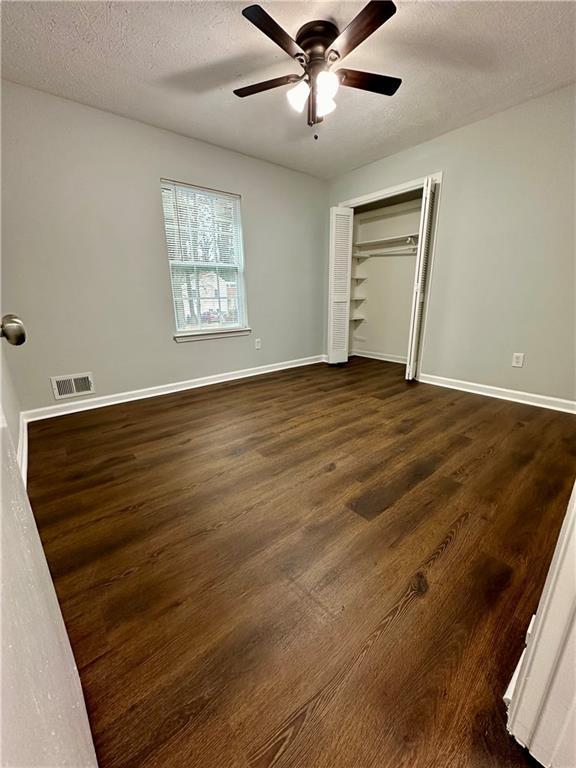 unfurnished bedroom featuring dark hardwood / wood-style flooring, a textured ceiling, ceiling fan, and a closet