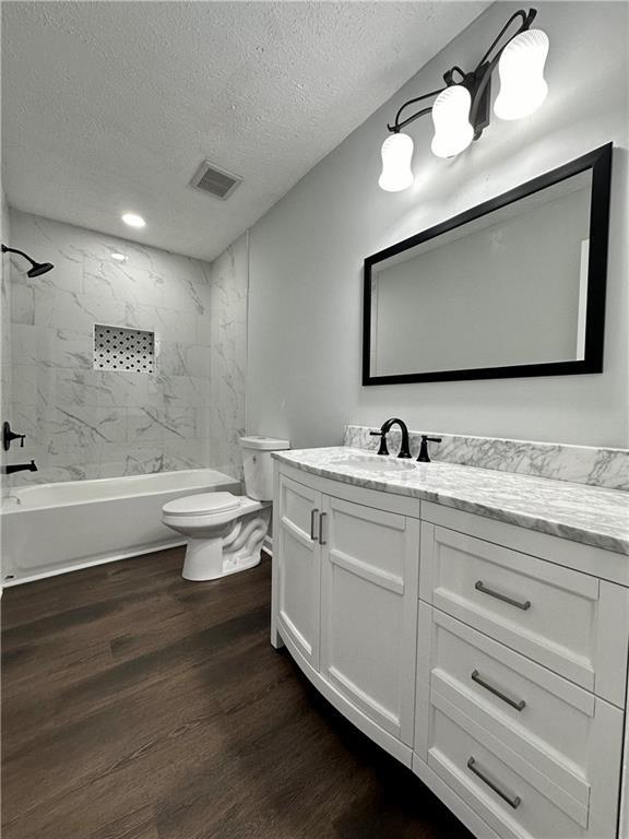 full bathroom featuring toilet, tiled shower / bath, a textured ceiling, vanity, and hardwood / wood-style floors