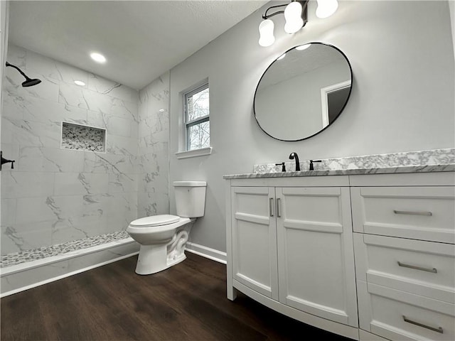 bathroom featuring hardwood / wood-style flooring, tiled shower, vanity, and toilet