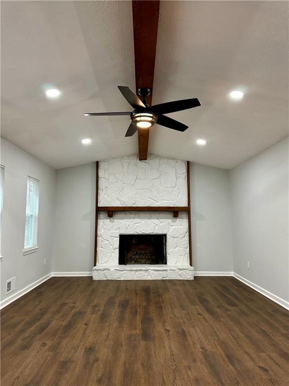 unfurnished living room featuring lofted ceiling with beams, a stone fireplace, dark wood-type flooring, and ceiling fan