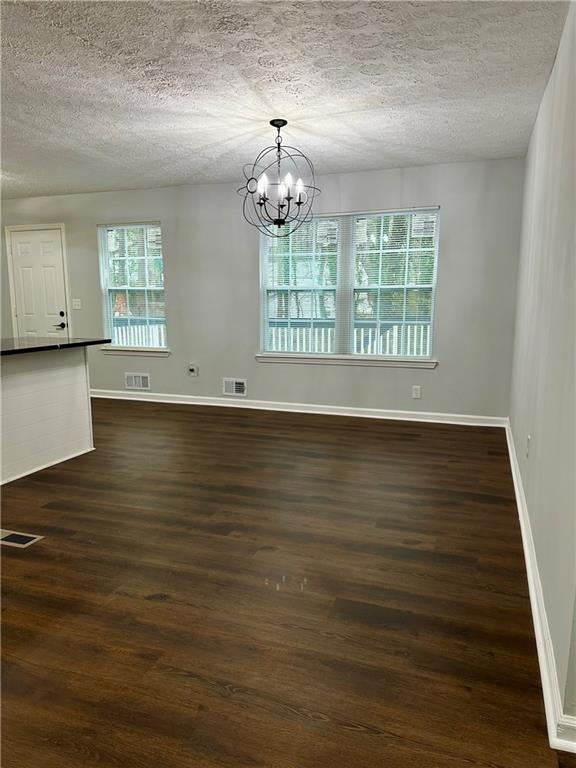 spare room featuring dark wood-type flooring, a textured ceiling, and a notable chandelier