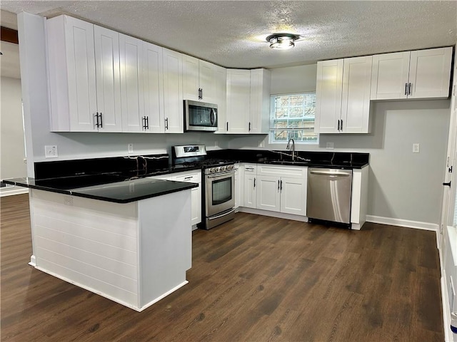 kitchen with dark wood-type flooring, appliances with stainless steel finishes, a textured ceiling, white cabinets, and kitchen peninsula