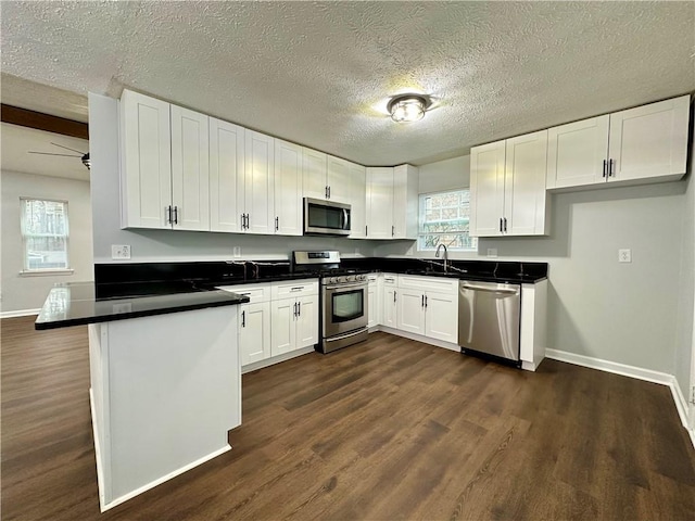 kitchen with appliances with stainless steel finishes, dark hardwood / wood-style floors, white cabinetry, kitchen peninsula, and a textured ceiling