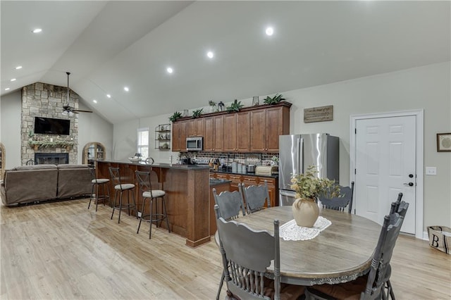 dining room featuring vaulted ceiling, a stone fireplace, ceiling fan, and light hardwood / wood-style flooring