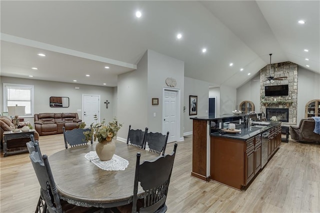 dining room with ceiling fan, lofted ceiling, light wood-type flooring, and a fireplace