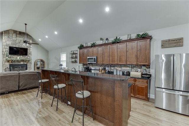 kitchen with lofted ceiling, light hardwood / wood-style flooring, appliances with stainless steel finishes, a fireplace, and a kitchen bar