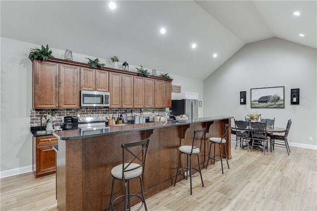 kitchen with tasteful backsplash, appliances with stainless steel finishes, a kitchen island, and light hardwood / wood-style flooring