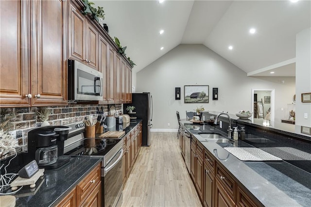 kitchen with sink, dark stone countertops, decorative backsplash, light hardwood / wood-style floors, and stainless steel appliances