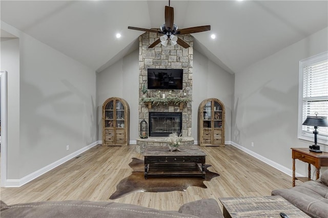 living room with ceiling fan, a stone fireplace, high vaulted ceiling, and light hardwood / wood-style flooring