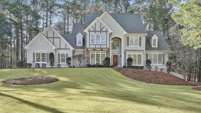 tudor home featuring stucco siding, a front lawn, and a shingled roof