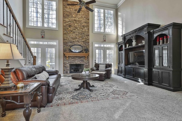 carpeted living area with stairway, ceiling fan, a stone fireplace, french doors, and crown molding