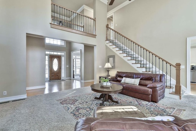 carpeted living room with a towering ceiling, baseboards, wood finished floors, and stairs