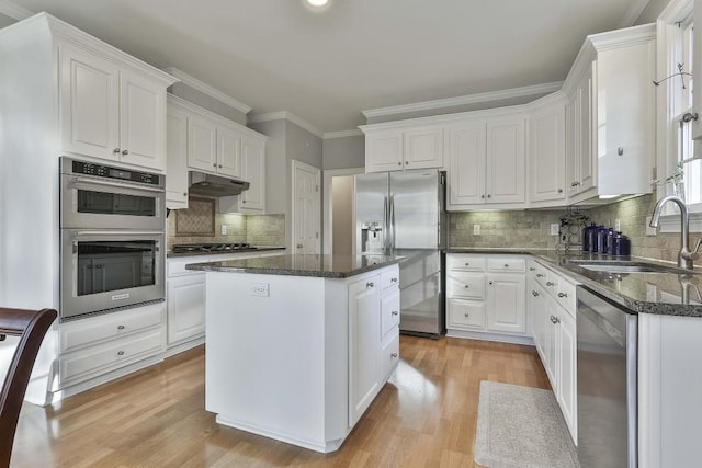 kitchen with a sink, under cabinet range hood, a kitchen island, white cabinetry, and stainless steel appliances