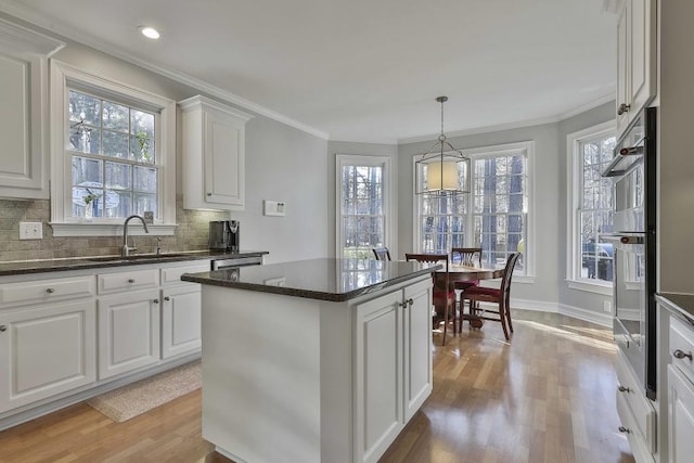 kitchen featuring tasteful backsplash, a center island, crown molding, light wood-style flooring, and a sink