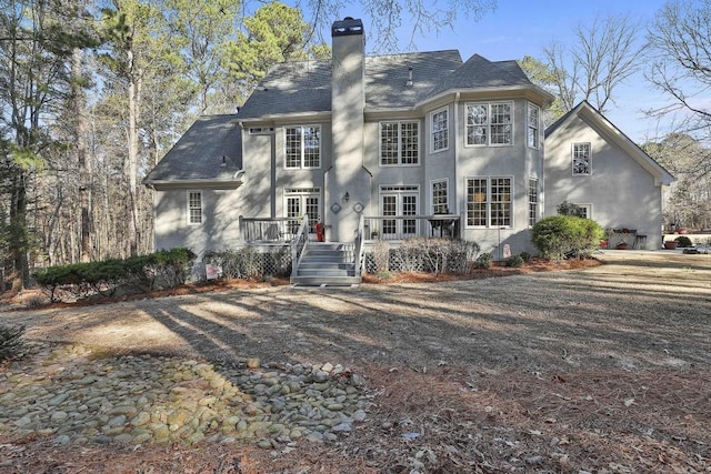 rear view of house with stucco siding, a chimney, and a deck