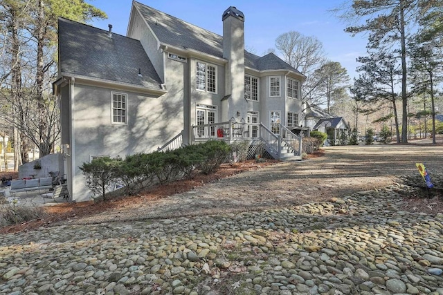 exterior space with a chimney, roof with shingles, and stucco siding