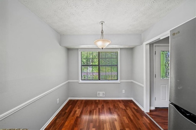 unfurnished dining area with a textured ceiling, wood finished floors, visible vents, and baseboards