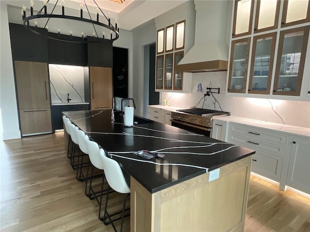 kitchen featuring white cabinetry, a breakfast bar area, a kitchen island with sink, and custom exhaust hood