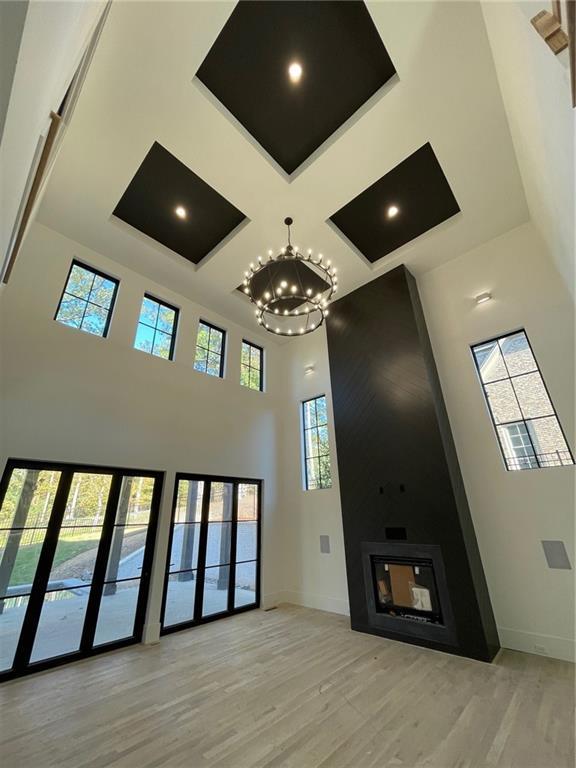 unfurnished living room featuring coffered ceiling, a towering ceiling, a chandelier, and light wood-type flooring