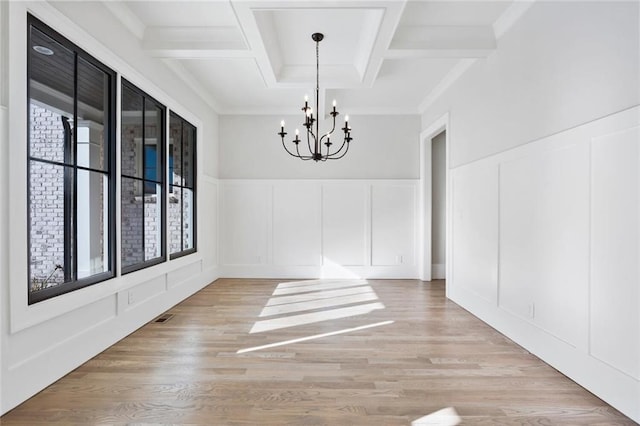 unfurnished dining area featuring coffered ceiling, a notable chandelier, beam ceiling, and light hardwood / wood-style flooring