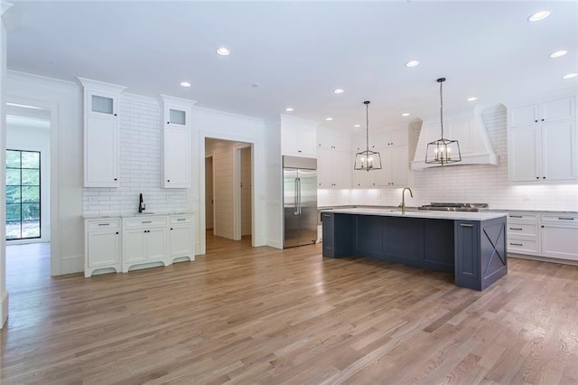 kitchen featuring an island with sink, white cabinets, and built in refrigerator