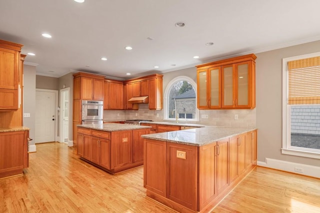 kitchen featuring light stone countertops, ornamental molding, kitchen peninsula, light wood-type flooring, and stainless steel gas stovetop