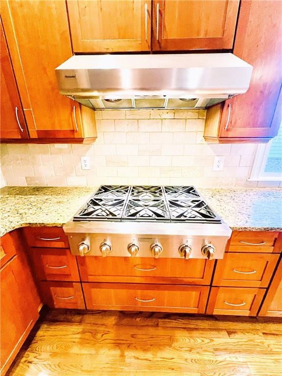 kitchen with stainless steel gas cooktop, light hardwood / wood-style flooring, backsplash, and light stone countertops