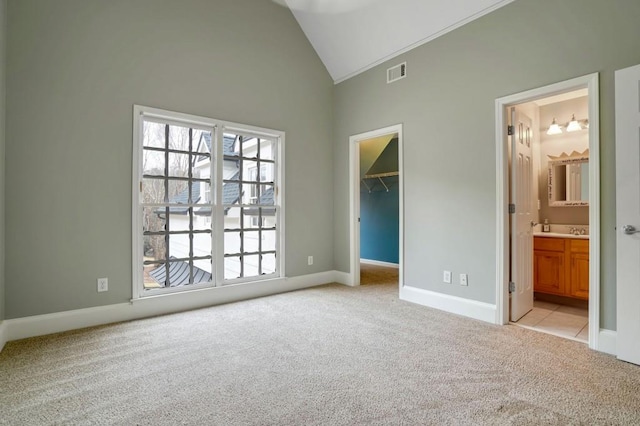 unfurnished bedroom with a walk in closet, ensuite bath, a closet, high vaulted ceiling, and light colored carpet