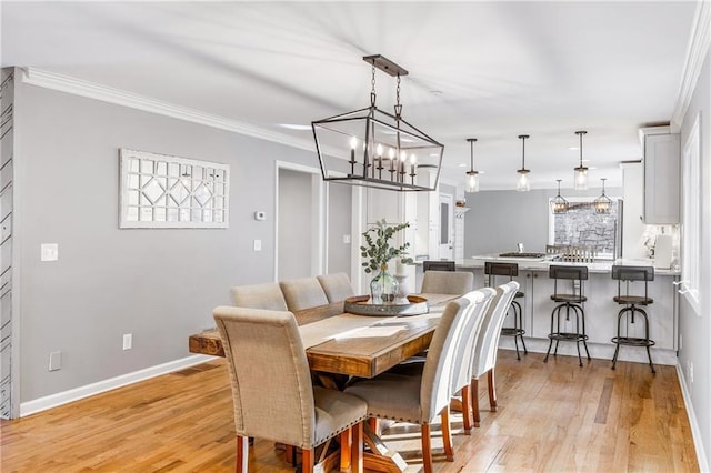 dining room with baseboards, a chandelier, crown molding, and light wood finished floors