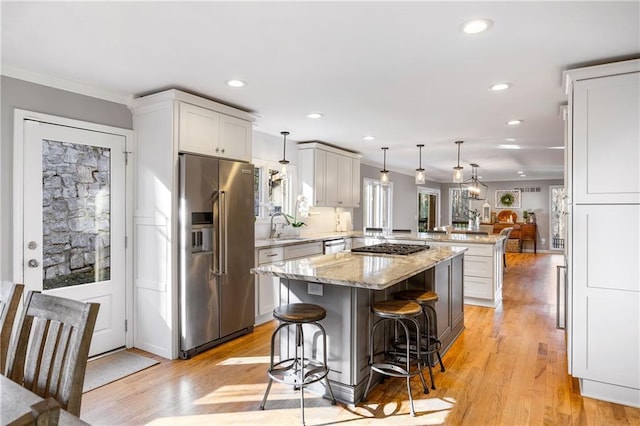 kitchen with light wood-type flooring, light stone counters, appliances with stainless steel finishes, a peninsula, and crown molding