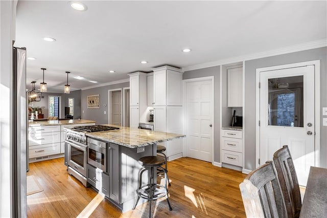 kitchen featuring light wood finished floors, crown molding, light stone countertops, a breakfast bar area, and stainless steel range