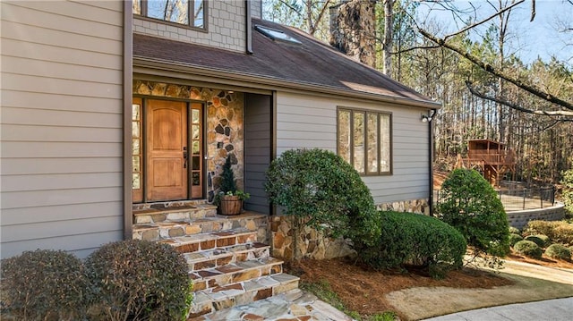 doorway to property featuring stone siding and a shingled roof