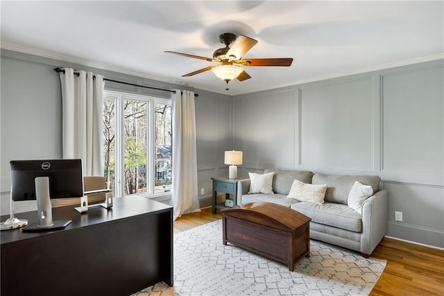 living area featuring a decorative wall, ornamental molding, light wood-style flooring, and ceiling fan