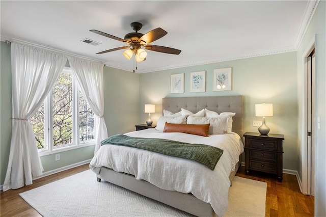 bedroom featuring wood finished floors, visible vents, and ornamental molding