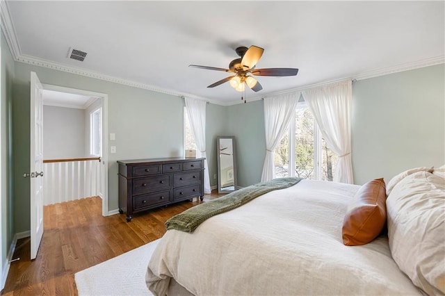 bedroom featuring wood finished floors, baseboards, visible vents, ceiling fan, and ornamental molding