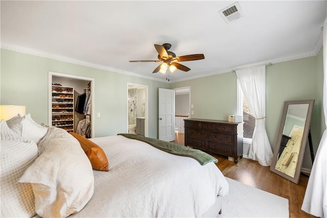 bedroom featuring visible vents, wood finished floors, a spacious closet, and crown molding