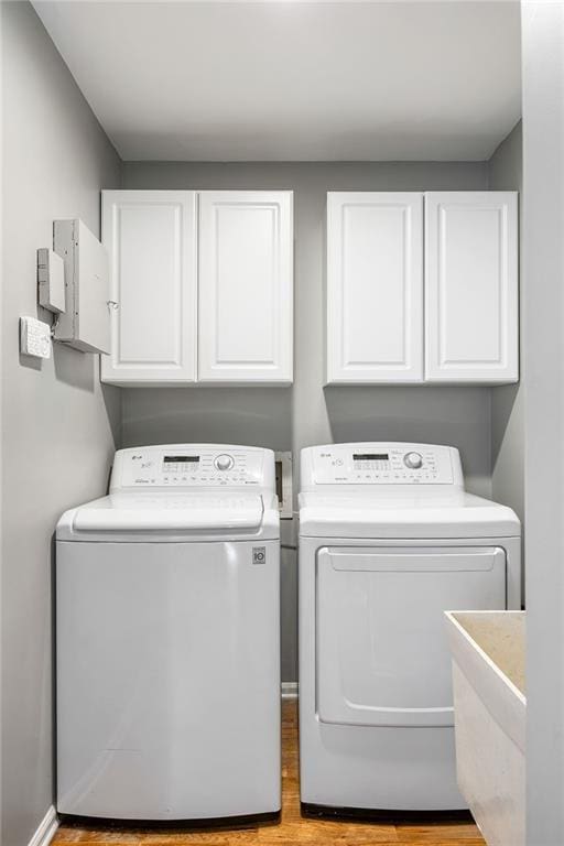 laundry area with washing machine and clothes dryer, cabinet space, light wood-type flooring, and a sink