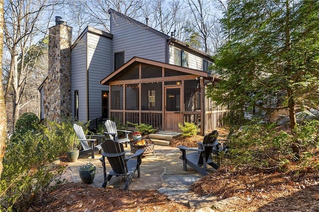 rear view of property featuring a patio area, a chimney, an outdoor fire pit, and a sunroom