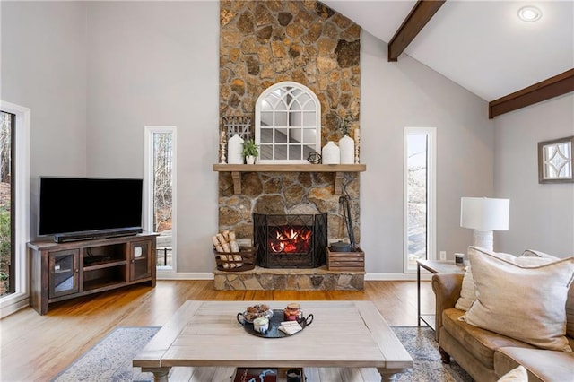 living room featuring beamed ceiling, high vaulted ceiling, a stone fireplace, and wood finished floors